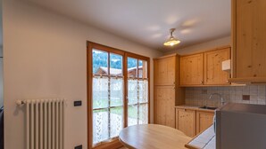 A kitchen with wooden cabinets, a built-in refrigerator, a window with frosted glass, and a radiator. - Casa De La Veisc (Pozza di Fassa)