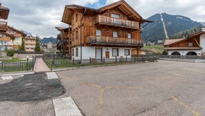 A wooden building with balconies, a paved area, and mountains in the background. - Casa De La Veisc (Pozza di Fassa)