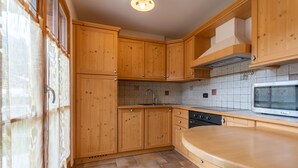 A kitchen with wooden cabinets, a tiled backsplash, a built-in oven, and a microwave. - Casa De La Veisc (Pozza di Fassa)