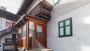 A residential building with a wooden front door, a balcony with a railing, and a stone staircase leading to the entrance. - Casa Cristina (Campitello di Fassa)