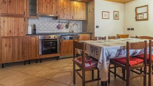 A kitchen with wooden cabinets, a stove, and a dining table with chairs. - Casa Cristina (Campitello di Fassa)