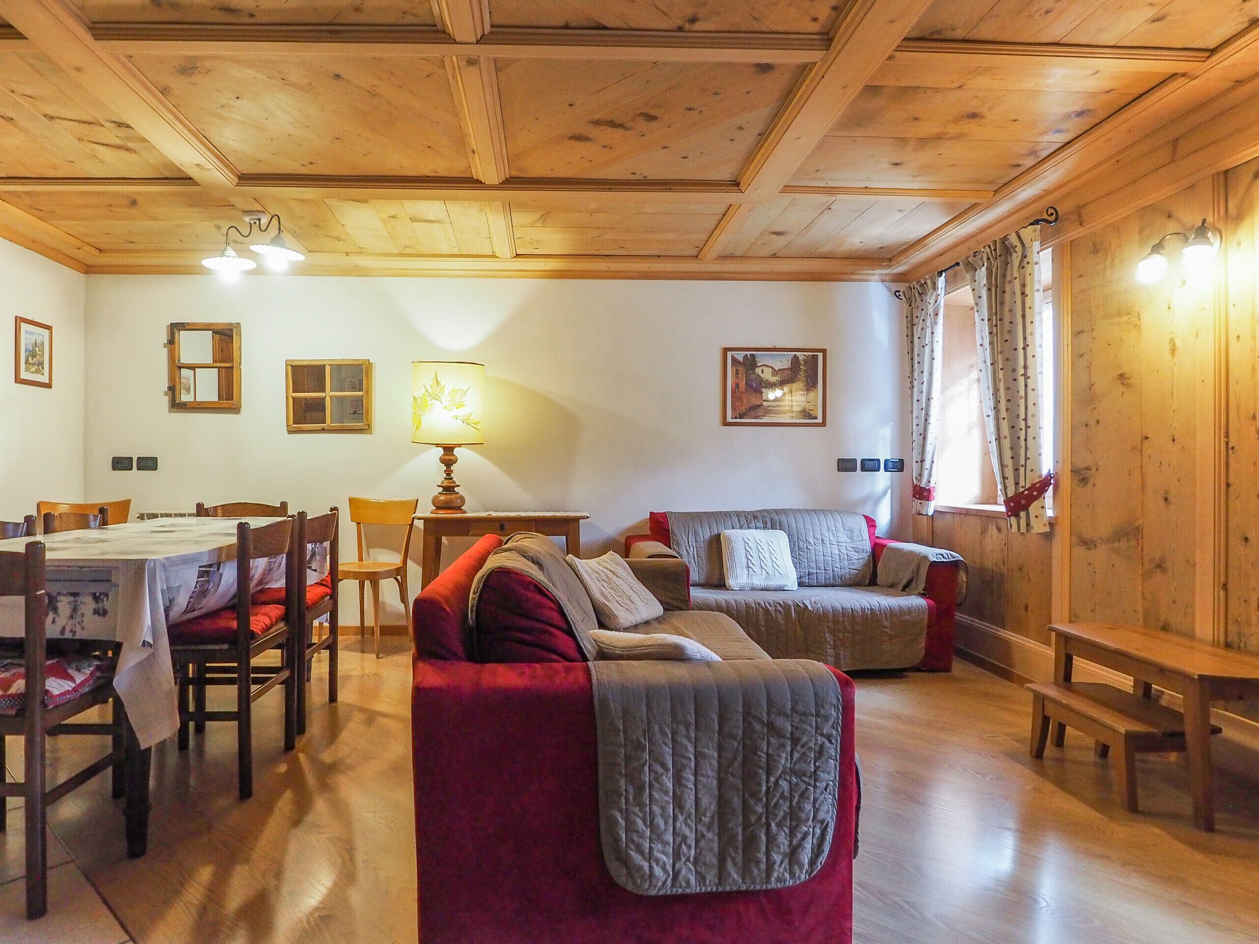 A cozy room with wooden ceilings, a dining table, chairs, a sofa, and a lamp.