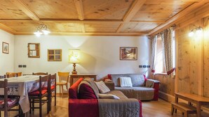 A cozy room with wooden ceilings, a dining table, chairs, a sofa, and a lamp. - Casa Cristina (Campitello di Fassa)