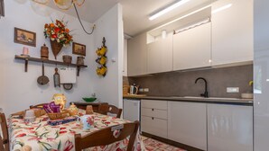 Een moderne keuken met witte kasten, een eethoek met een tafelkleed met bloemen, en een wandmandje met bloemen.