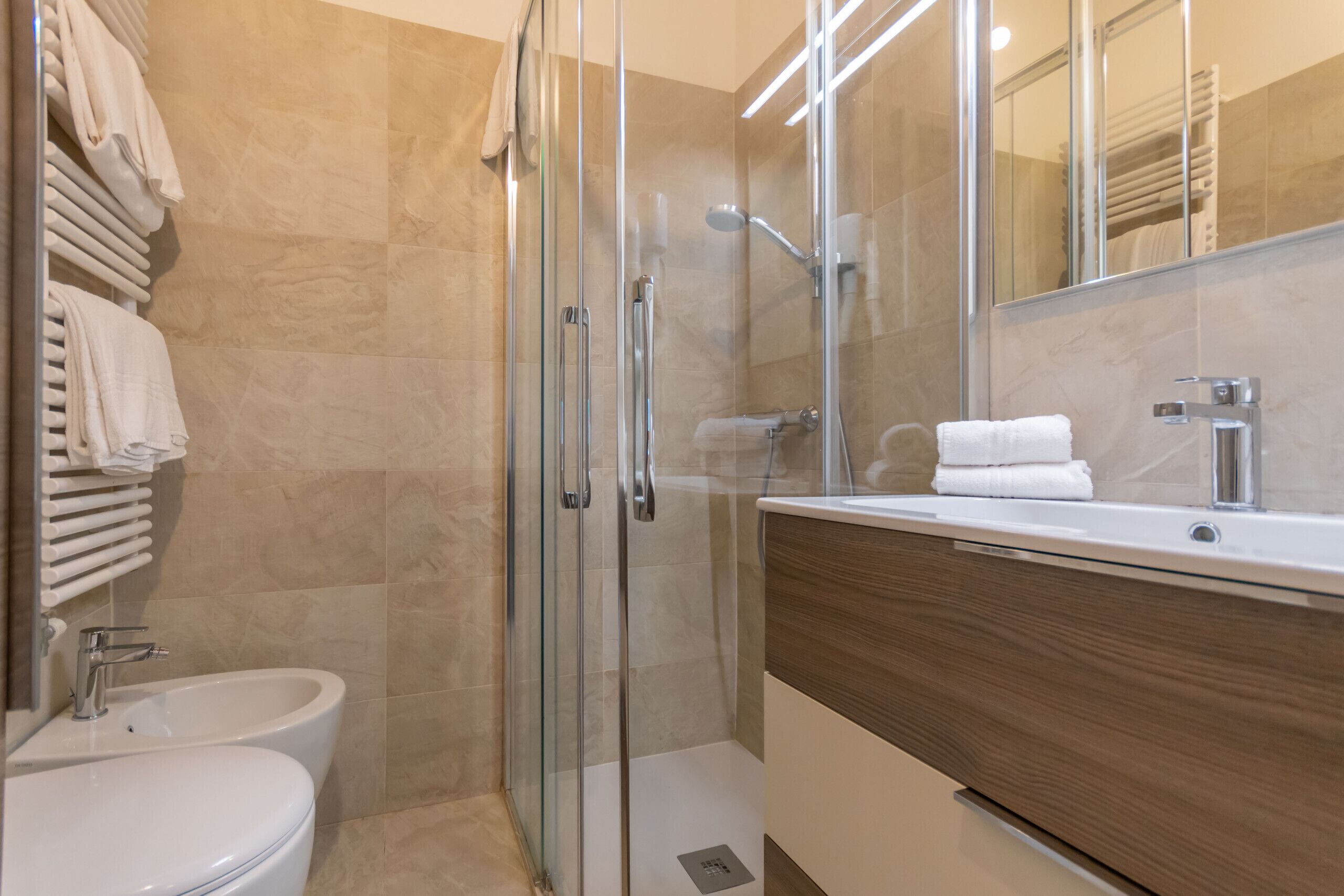 A modern bathroom with a glass-enclosed shower, a white sink, and a wooden vanity.