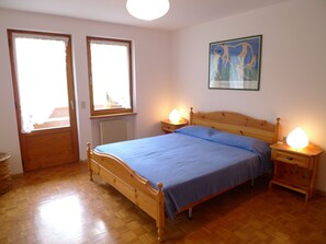 Un dormitorio con una cama de madera, dos lámparas de noche, un radiador y una ventana con vistas.