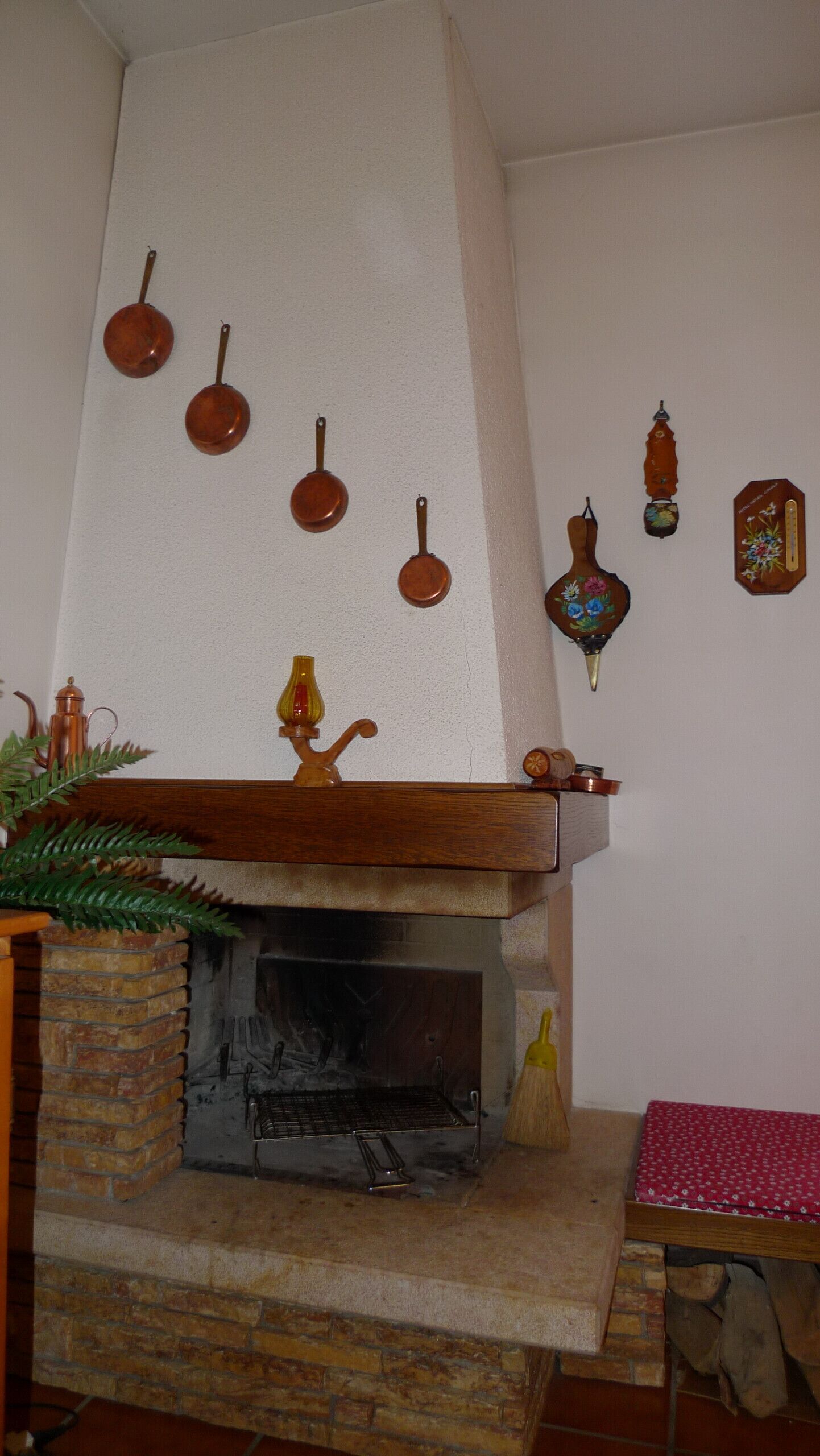 Een open haard met een stenen bovenkant, een bakstenen muur en een houten plank met diverse decoratieve objecten.