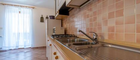 A kitchen with a gas stove, two sinks, and a tiled backsplash.