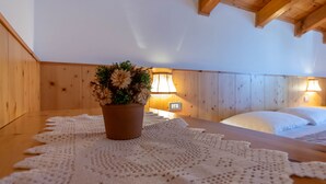 Een knus vertrek met houten wanden, een houten plafond, een bed met witte beddengoed, een nachtkastje met een potplant en twee wandlampen.