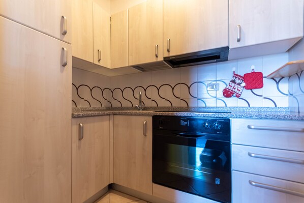 A kitchen with light wooden cabinets, a black dishwasher, and a stainless steel oven.