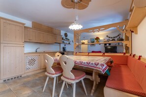 A cozy kitchen with wooden cabinets, a dining table with chairs, and a red cushioned bench. - Casa Rosi (Pozza di Fassa)