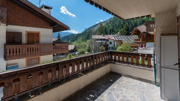 A balcony with a stone floor, wooden railings, and a view of a mountain and buildings.