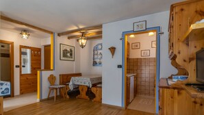 A cozy room with wooden floors, a bed, a small table with a chair, and a bathroom with a shower and sink.