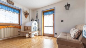 A cozy room with a wooden floor, a sofa, a radiator, a window with curtains, and a wall-mounted lamp.