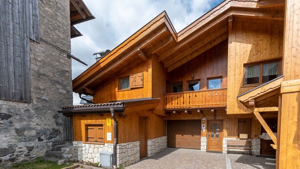 Una cabaña de madera con base de piedra, un balcón y un garaje.