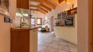 Una cocina con vigas de madera, piso de baldosas, horno empotrado y un comedor con mesa y sillas.