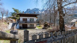 Un chalet à deux étages doté d’un balcon, entouré d’une clôture en bois et surplombant un paysage montagneux.