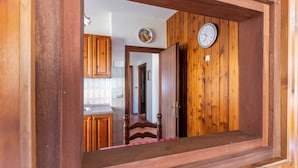 Un passage encadré de bois mène à une cuisine dotée de meubles en bois et d’une horloge murale.