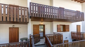 A wooden balcony with a railing, a staircase leading to an upper level, and a door with a window.