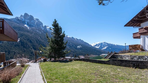 A pathway leading to a mountain view with a stone wall and wooden buildings.