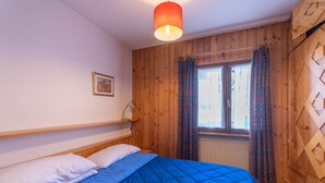 A bedroom with a bed, wooden walls, a window with curtains, and a radiator.