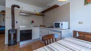 A compact kitchen with a stove, oven, microwave, and a small dining area with a table and chair. - Dimora al Villaggio (Mazzin)