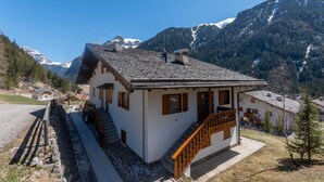 A traditional chalet with a stone staircase, wooden balcony, and a view of snow-capped mountains. - Dimora al Villaggio (Mazzin)