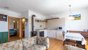 A cozy living room with a floral sofa and a dining area with a table and chairs. A kitchen with a microwave and a sink is visible in the background. - Dimora al Villaggio (Mazzin)