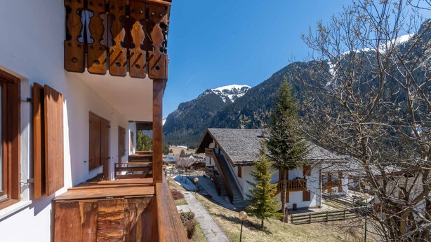 A wooden balcony with a view of a mountain and a traditional chalet. - Dimora al Villaggio (Mazzin)