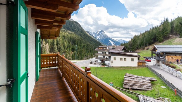 Un balcon en bois offrant une vue sur un paysage montagneux, avec des maisons et une route.