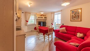 Un salon avec un canapé rouge, une table à manger avec des chaises et un coin cuisine équipé d’un four à micro-ondes et d’une fenêtre.