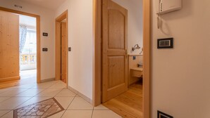 Un couloir avec des portes en bois, un sol carrelé et une petite salle de bain équipée d’un lavabo et d’un miroir.