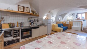 Een kleine keuken met witte kastjes, een vaatwasser en een eethoek met een tafel bedekt met een tafelkleed met hartjes.