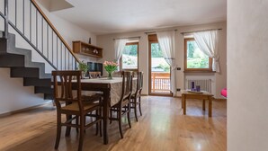 Ein Essbereich mit Holzkreislern und einem Tisch, eine Treppe und ein Blick ins Freie durch ein Fenster.