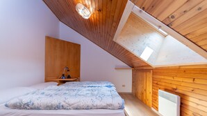 A bedroom with a sloped ceiling, wooden walls, a bed with a floral duvet, a bedside table with a lamp, and a radiator.