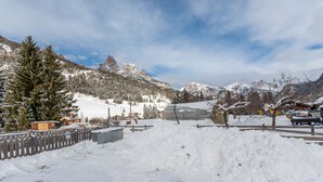 A snowy mountain landscape with a wooden fence, a parked car, and a building with a snow-covered roof.