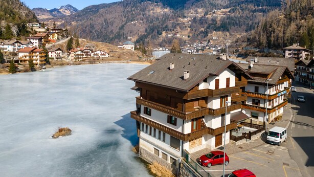 A multi-story building with a traditional architectural style, located near a frozen lake with a mountainous backdrop. - Appartamento Miralago (Alleghe)