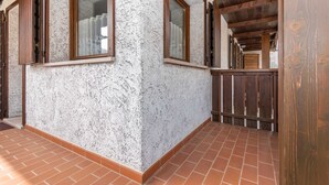 Une pièce avec un mur blanc à la texture particulière, des poutres en bois et un sol carrelé.