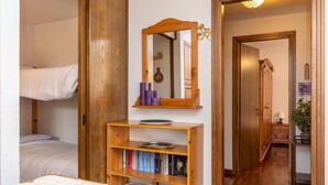Une chambre avec un lit superposé, une bibliothèque en bois, un miroir et un couloir menant à une salle de bain.