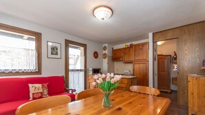 Un coin repas avec une table et des chaises en bois, un vase de tulipes, un canapé rouge agrémenté de coussins décoratifs et, au fond, des meubles en bois.