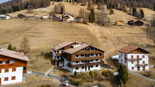 Un village de montagne aux maisons traditionnelles en bois, sous un ciel dégagé, avec une montagne imposante en arrière-plan.