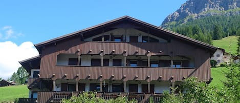 A multi-story building with balconies, set against a mountainous backdrop.
