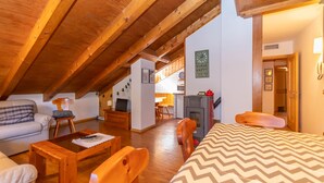 A cozy attic bedroom with wooden beams, a bed, a desk, and a fireplace.