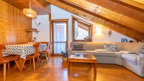 A cozy attic living room with wooden beams, a sofa, a dining table with benches, and a hanging light fixture.