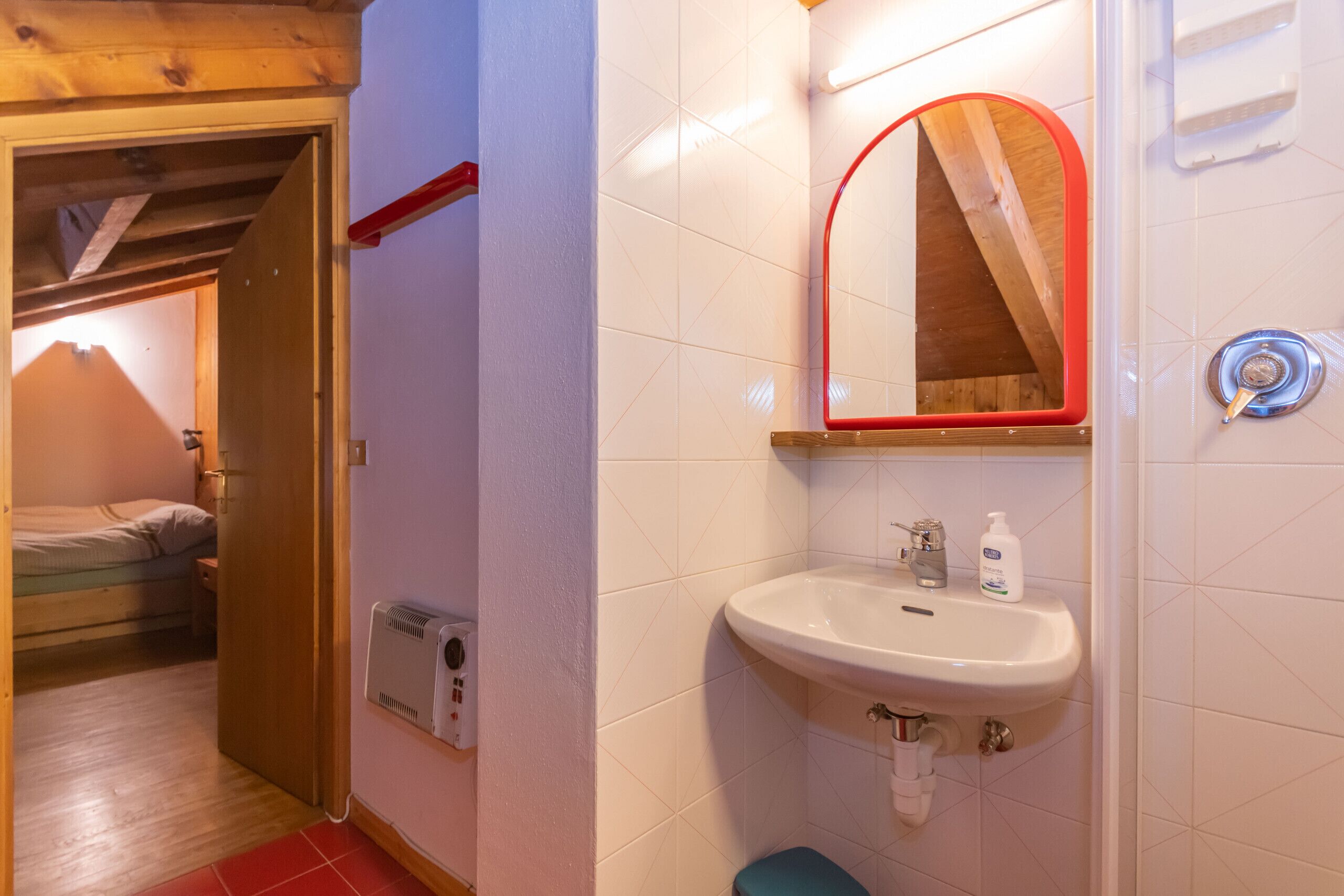 Een badkamer met een wit wastafel, een spiegel met rode rand, en een douchehoek.