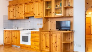 A kitchen with wooden cabinets, a stove, a sink, and a TV. - Casa Maura (Soraga)