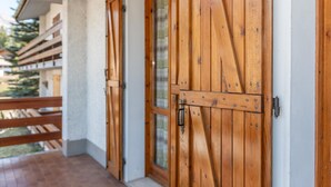 A wooden door with a metal handle and a glass panel, leading to a covered outdoor area with a wooden railing.