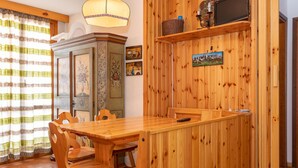 A wooden dining area with a table and chairs, a cabinet with artwork, and a shelf with decorative items.