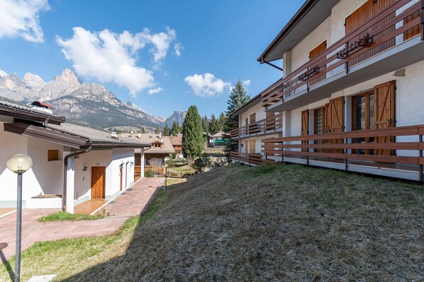 A hillside building with a wooden balcony, a clear sky, and mountains in the background.