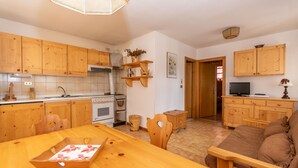 A kitchen with wooden cabinets, a dining table with a box, and a sofa in the living area. - Casa Coli (Mazzin)